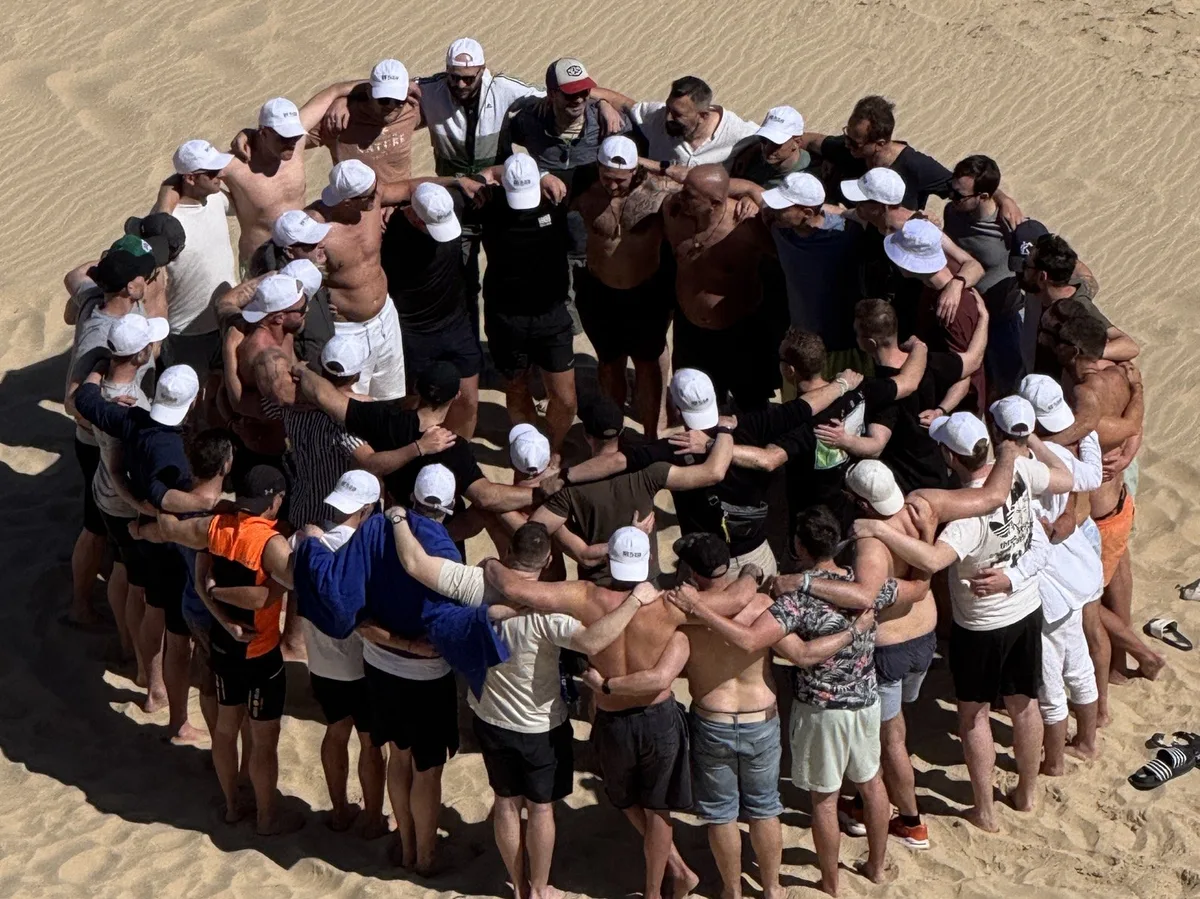 Die Gruppe steht im Kreis im Sand, von oben fotografiert